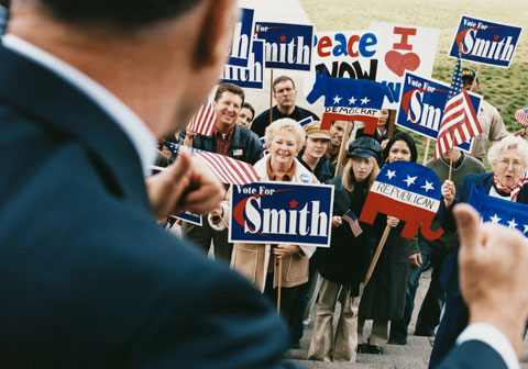 politician thumbs up at crowd with republican and vote for smith signs