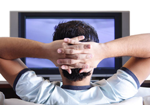 Man watching TV with hands crossed behind head