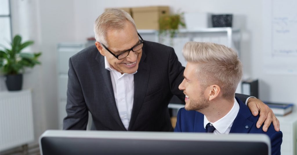 manager smiling with hand on shoulder of employee at their desk